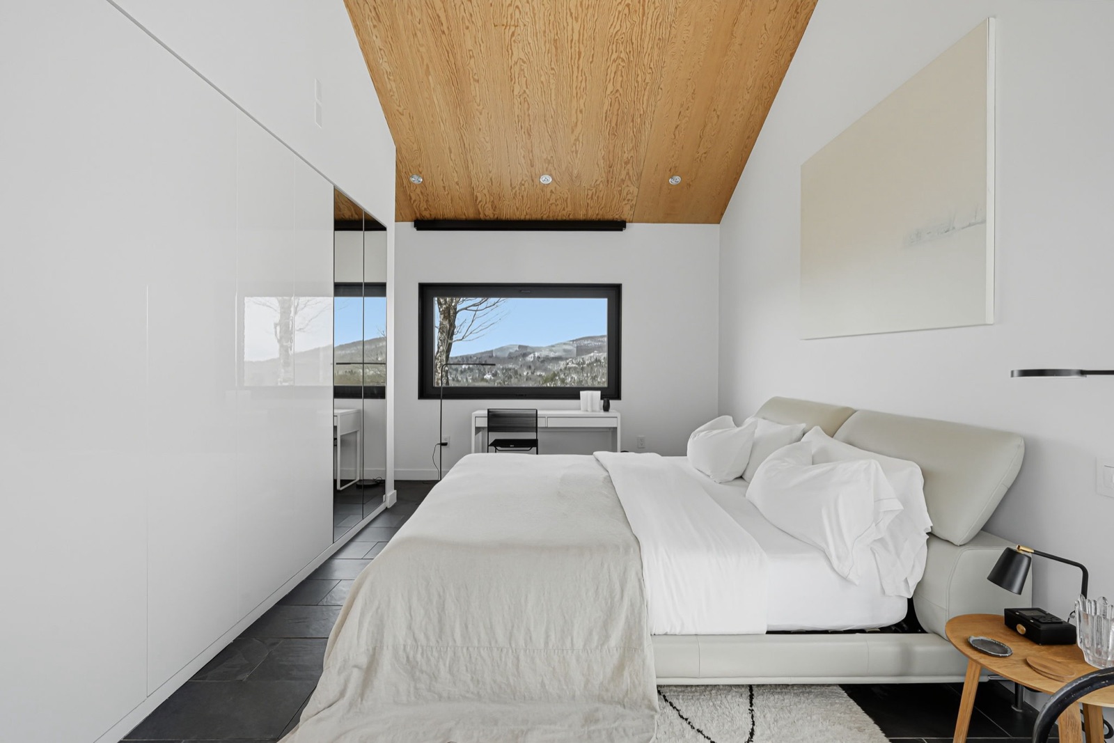 Chambre principale : lit, garde-robe blanche et fenêtre sur les montagnes