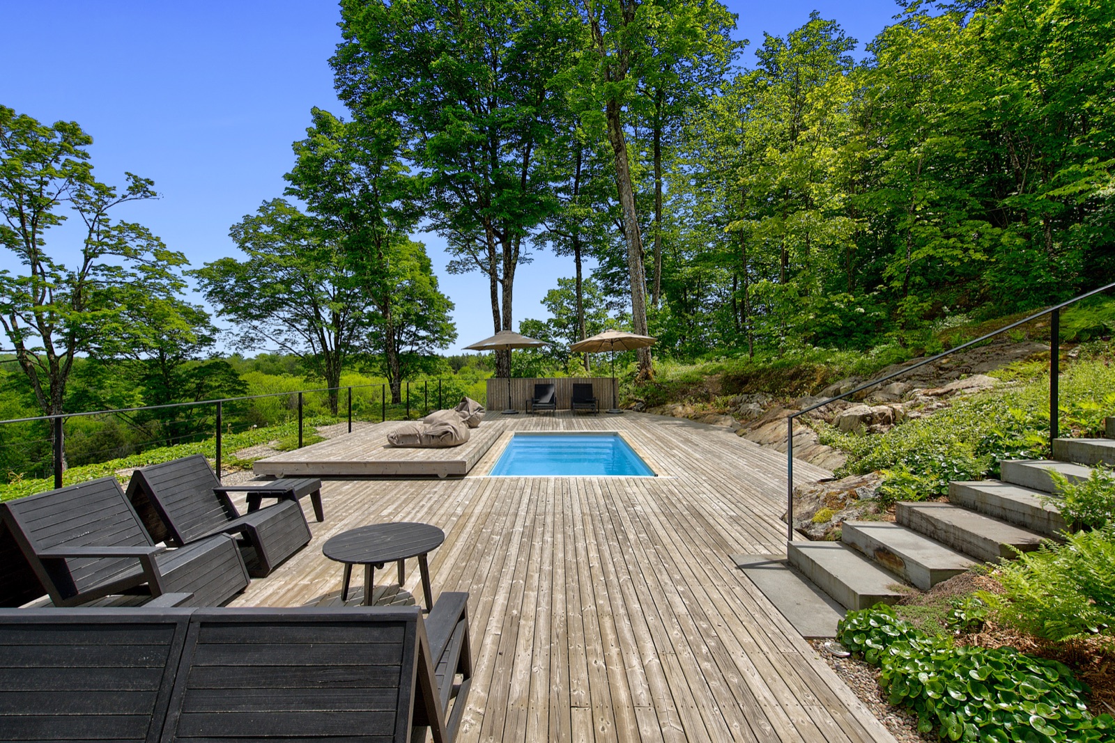 Terrasse en bois et piscine creusée entourées de verdure