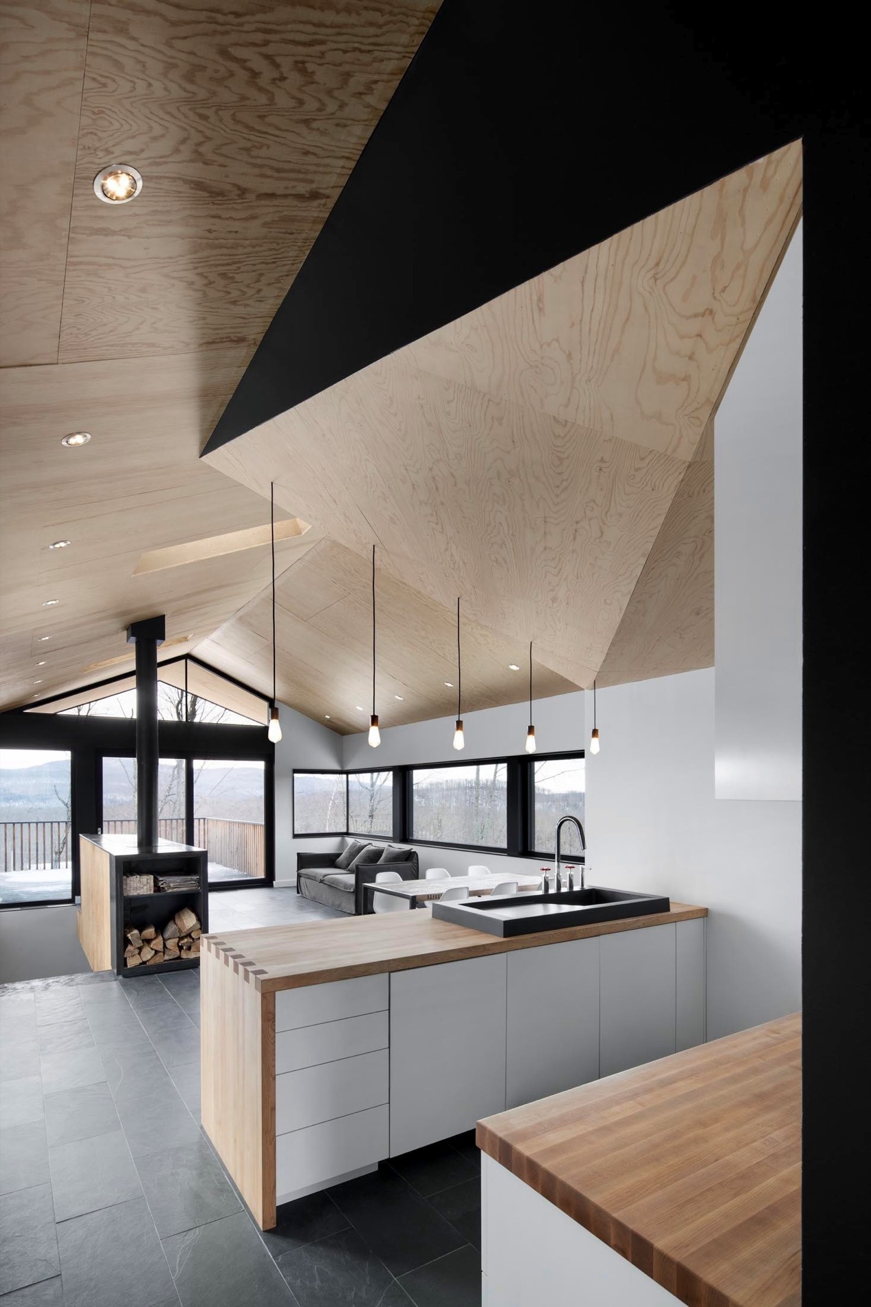 Cuisine ouverte : plafond en contreplaqué, lampes suspendues, comptoir en bois et foyer au fond